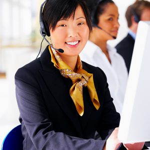 Portrait of a beautiful helpdesk or support line operator answering a call, with her colleagues in the background.
